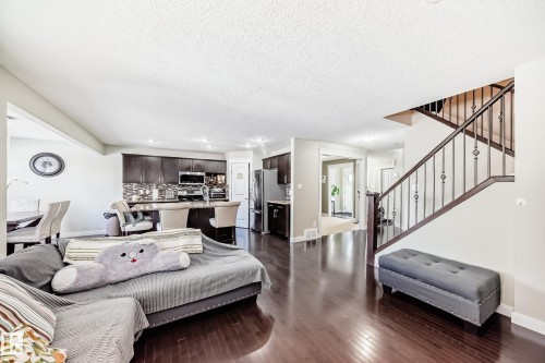 The property features rich hardwood flooring, a staircase with decorative metal spindles, and a kitchen with dark cabinetry and a tiled backsplash - 3433 Goodridge Link Link, Edmonton, AB - Indoor Photo Showing Living Room
