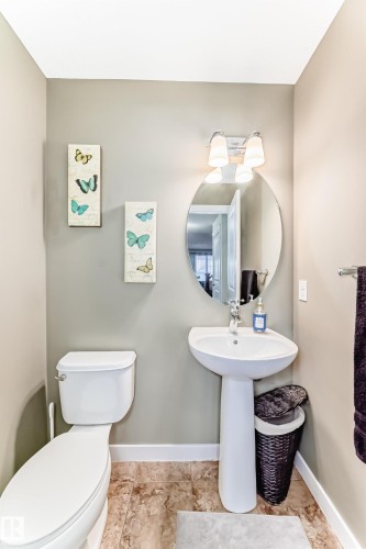 The bathroom features a white pedestal sink, a toilet, and a circular mirror with an overhead light fixture - 3433 Goodridge Link Link, Edmonton, AB - Indoor Photo Showing Bathroom