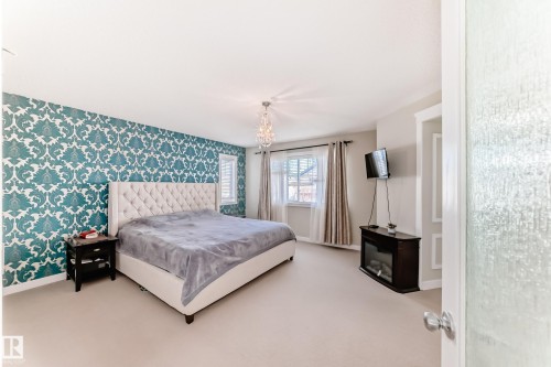 Bedroom featuring a stylish accent wall with patterned wallpaper, a tufted headboard, and a window with curtains - 3433 Goodridge Link Link, Edmonton, AB - Indoor Photo Showing Bedroom