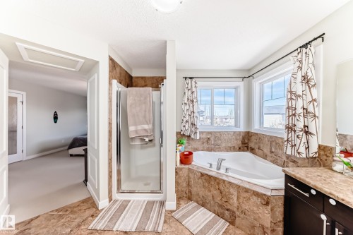 Bathroom featuring a corner soaking tub with windows above, a glass-enclosed shower, and a vanity with a countertop - 3433 Goodridge Link Link, Edmonton, AB - Indoor Photo Showing Bathroom