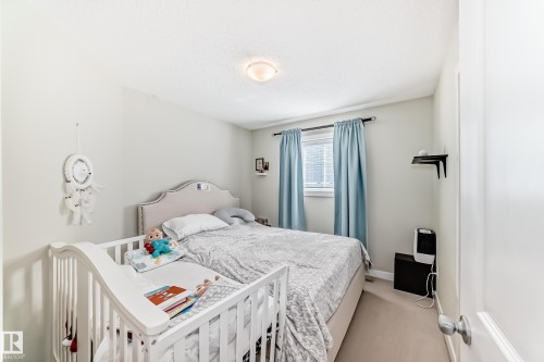 This bedroom features a window with blinds and blue curtains, a light-colored carpet, and a light fixture on the ceiling - 3433 Goodridge Link Link, Edmonton, AB - Indoor Photo Showing Bedroom