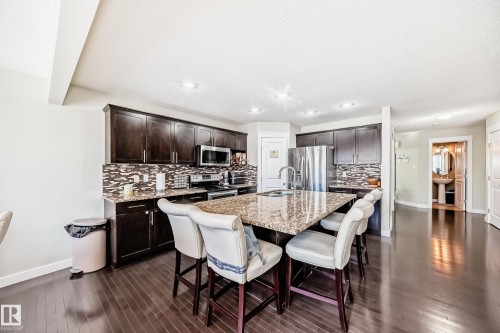 The kitchen features dark wood cabinetry, stainless steel appliances, a large center island with granite countertops, and dark hardwood floors - 3433 Goodridge Link Link, Edmonton, AB - Indoor