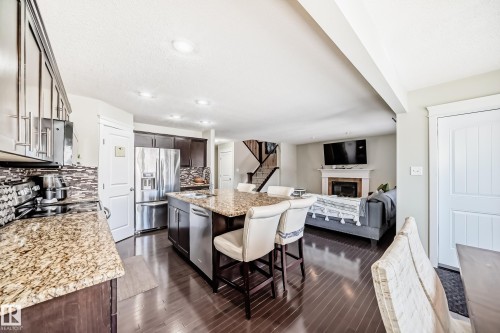 Open-concept living space with dark wood flooring, a kitchen featuring granite countertops and stainless steel appliances, and a living area with a fireplace - 3433 Goodridge Link Link, Edmonton, AB - Indoor With Fireplace