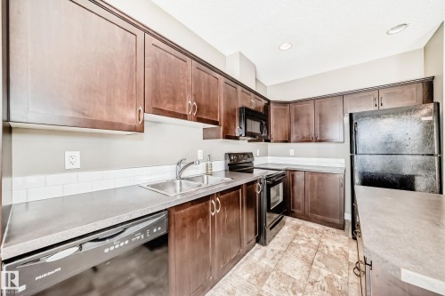 The kitchen features dark wood cabinetry, a double basin sink, and black appliances including a refrigerator, oven, and dishwasher - 44 13825 155 Avenue, Edmonton, AB - Indoor Photo Showing Kitchen With Double Sink