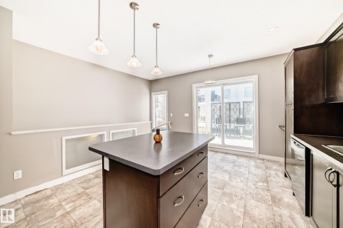 The kitchen features an island with dark cabinetry and a dark countertop, complemented by light-colored tiled flooring - 44 13825 155 Avenue, Edmonton, AB - Indoor