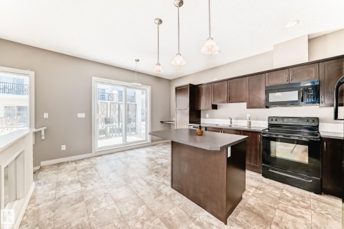 The kitchen features dark wood cabinetry, a central island, and black appliances including a stove and microwave - 44 13825 155 Avenue, Edmonton, AB - Indoor Photo Showing Kitchen With Double Sink