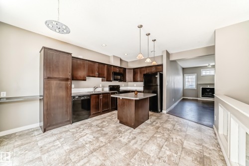 The kitchen features dark wood cabinetry, a central island with a countertop, and black appliances - 44 13825 155 Avenue, Edmonton, AB - Indoor Photo Showing Kitchen