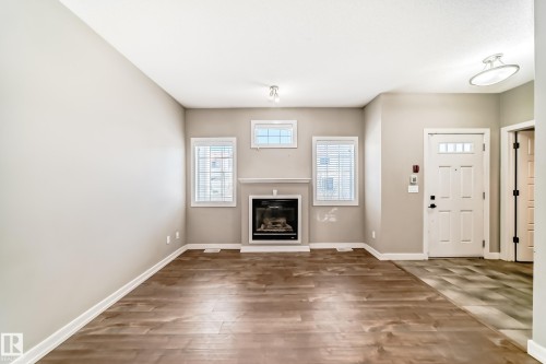 Living room featuring wide plank flooring, a fireplace with a mantel, and two windows with blinds - 44 13825 155 Avenue, Edmonton, AB - Indoor With Fireplace