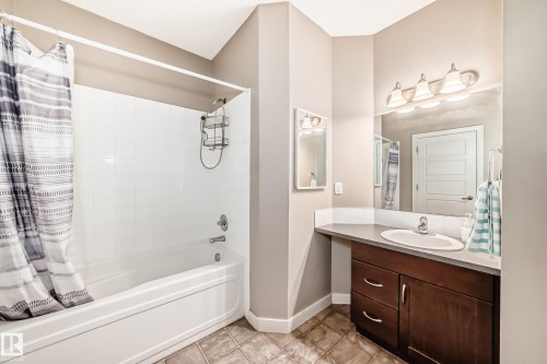 Bathroom featuring a white bathtub with a tiled surround, a vanity with a white countertop and dark wood cabinetry, and a large mirror with a four-light fixture - 44 13825 155 Avenue, Edmonton, AB - Indoor Photo Showing Bathroom