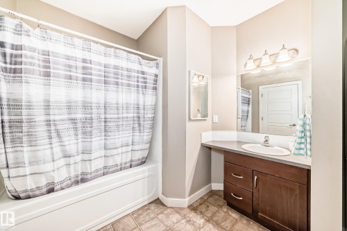 Bathroom featuring a built-in bathtub with shower, a vanity with a white basin and chrome faucet, a large mirror, and tiled flooring - 44 13825 155 Avenue, Edmonton, AB - Indoor Photo Showing Bathroom