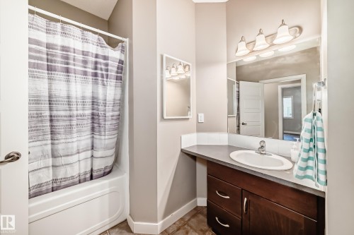 Bathroom with a vanity featuring a single basin sink, a large mirror, and a wall-mounted light fixture - 44 13825 155 Avenue, Edmonton, AB - Indoor Photo Showing Bathroom