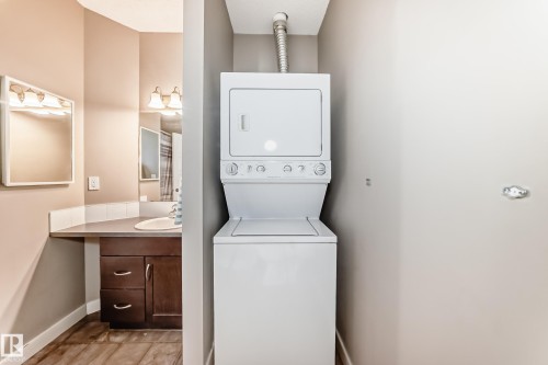 Convenient laundry area with a stackable washer and dryer unit, located near a bathroom featuring a vanity with a countertop, sink, and mirror - 44 13825 155 Avenue, Edmonton, AB - Indoor Photo Showing Laundry Room