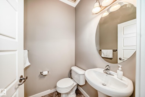 A well-appointed bathroom featuring a pedestal sink, a toilet, and an oval mirror with a three-bulb vanity light fixture - 44 13825 155 Avenue, Edmonton, AB - Indoor Photo Showing Bathroom