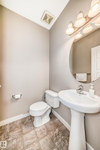 The bathroom features a pedestal sink, a toilet, a round mirror with overhead lighting, and tiled flooring - 44 13825 155 Avenue, Edmonton, AB - Indoor Photo Showing Bathroom