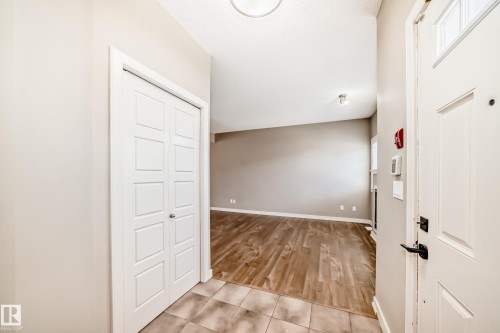 Entryway featuring tiled flooring, a coat closet with bi-fold doors, and a view into the main living area with wood-style flooring - 44 13825 155 Avenue, Edmonton, AB - Indoor Photo Showing Other Room