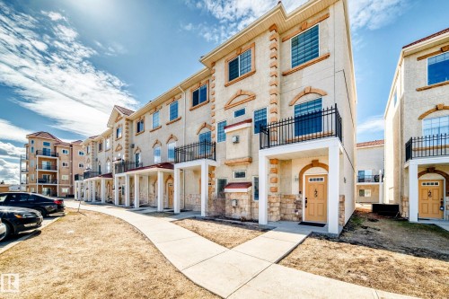 The property features a row of multi-level townhouses with balconies, arched windows, and light-colored stucco exteriors, complemented by a concrete walkway - 44 13825 155 Avenue, Edmonton, AB - Outdoor With Facade