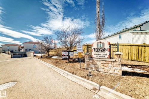 Entrance to Tuscan Village, featuring a stone and wrought iron sign, paved road, and established trees - 44 13825 155 Avenue, Edmonton, AB - Outdoor