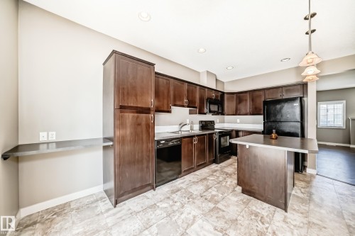 The kitchen features dark wood cabinetry, black appliances, and a central island with a countertop - 44 13825 155 Avenue, Edmonton, AB - Indoor Photo Showing Kitchen