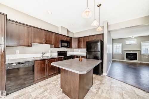 Kitchen featuring dark wood cabinetry, a central island with a grey countertop, and black appliances - 44 13825 155 Avenue, Edmonton, AB - Indoor Photo Showing Kitchen With Fireplace