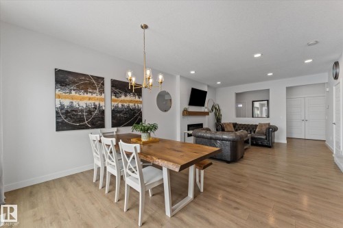 Spacious open-concept living area featuring light-toned flooring, a dining area with a rustic wooden table, and a living room with a fireplace - 13 Spring Link, Spruce Grove, AB - Indoor Photo Showing Other Room With Fireplace