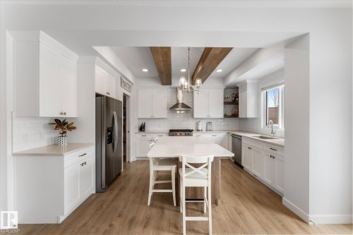 The property features a bright kitchen with white cabinetry, light wood flooring, and a central island with seating - 13 Spring Link, Spruce Grove, AB - Indoor Photo Showing Kitchen With Stainless Steel Kitchen With Upgraded Kitchen