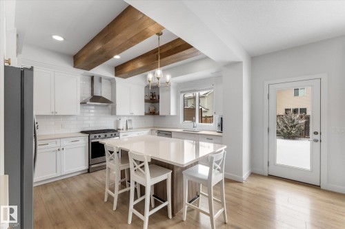 The kitchen features light-colored flooring, white cabinetry, a large central island with seating, a stainless steel range with a coordinating range hood, and a refrigerator - 13 Spring Link, Spruce Grove, AB - Indoor