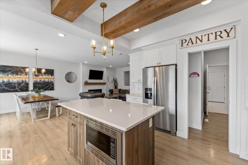 Open concept living area featuring a kitchen island with a built-in microwave, white shaker-style cabinetry, and a stainless steel refrigerator - 13 Spring Link, Spruce Grove, AB - Indoor Photo Showing Kitchen With Stainless Steel Kitchen With Upgraded Kitchen