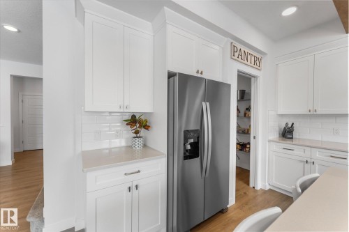 The kitchen features white cabinetry, a stainless steel refrigerator, and a pantry with shelving - 13 Spring Link, Spruce Grove, AB - Indoor Photo Showing Kitchen