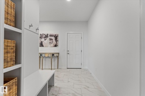 Hallway featuring light-colored tile flooring, a built-in storage unit with shelving, and wall-mounted coat hooks - 13 Spring Link, Spruce Grove, AB - Indoor Photo Showing Other Room