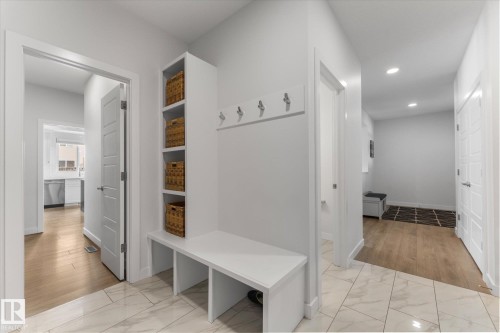 The entryway features white tiled flooring, a built-in storage bench with shelving, and wall-mounted coat hooks - 13 Spring Link, Spruce Grove, AB - Indoor Photo Showing Other Room