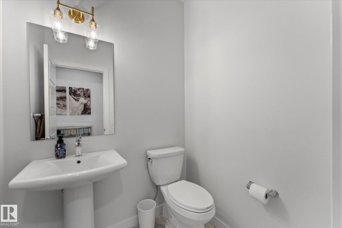 The bathroom features a pedestal sink with a rectangular mirror and an overhead light fixture with clear glass shades - 13 Spring Link, Spruce Grove, AB - Indoor Photo Showing Bathroom