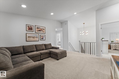 This versatile space features light-colored carpeting, recessed lighting, and a modern chandelier, providing an inviting atmosphere - 13 Spring Link, Spruce Grove, AB - Indoor Photo Showing Living Room