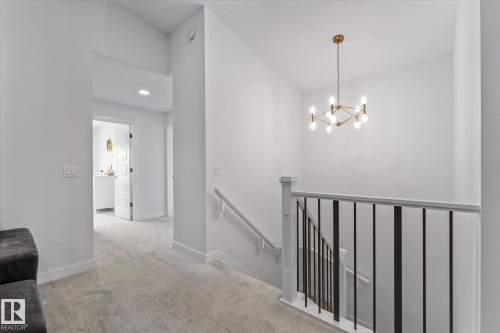 The property features a staircase with a white banister and black vertical balusters, illuminated by a chandelier with a gold-toned frame and exposed bulbs - 13 Spring Link, Spruce Grove, AB - Indoor Photo Showing Other Room