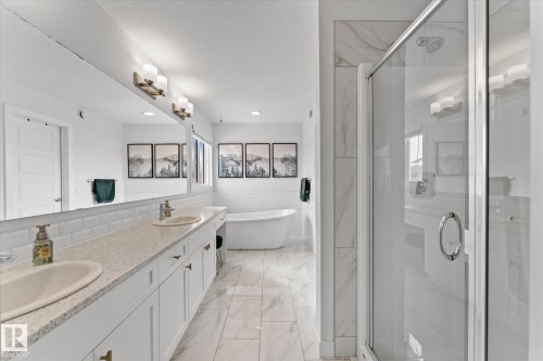 Bright bathroom featuring a large shower with a glass enclosure, a freestanding tub, and a vanity with dual sinks, white cabinetry, and a light-colored countertop - 13 Spring Link, Spruce Grove, AB - Indoor Photo Showing Bathroom
