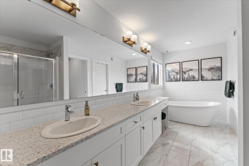 Spacious bathroom featuring a double vanity with granite countertops, a freestanding bathtub, a glass-enclosed shower, and large format tile flooring - 13 Spring Link, Spruce Grove, AB - Indoor Photo Showing Bathroom