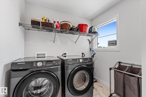 This laundry area features a window for natural light, a wall-mounted wire shelf, and tile flooring - 13 Spring Link, Spruce Grove, AB - Indoor Photo Showing Laundry Room