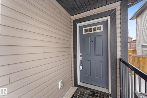 The property features light-colored horizontal siding and a contrasting dark gray paneled entry door with decorative glass inserts - 13 Spring Link, Spruce Grove, AB - Outdoor With Exterior