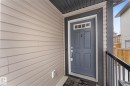 The property features light-colored horizontal siding and a contrasting dark gray paneled entry door with decorative glass inserts - 13 Spring Link, Spruce Grove, AB  - Outdoor With Exterior 
