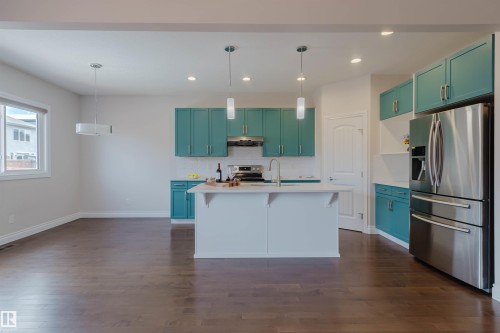 The kitchen features teal cabinetry, a center island with a sink, and stainless steel appliances including a refrigerator and range hood - 4875 Wright Drive, Edmonton, AB - Indoor Photo Showing Kitchen