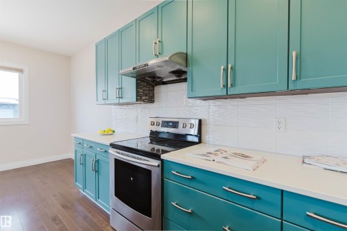 Kitchen featuring extensive teal cabinetry with brushed nickel hardware, white countertops, and a white tiled backsplash - 4875 Wright Drive, Edmonton, AB - Indoor Photo Showing Kitchen