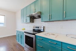 Kitchen featuring extensive teal cabinetry with brushed nickel hardware, white countertops, and a white tiled backsplash - 
