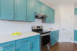 The kitchen features teal cabinetry, white countertops, and a white tiled backsplash - 
