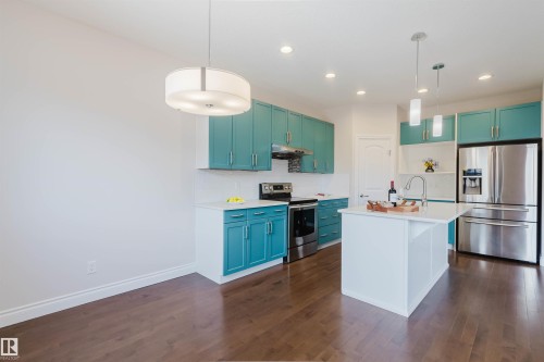 The kitchen features vibrant blue cabinetry, stainless steel appliances, a white island with a sink, and hardwood flooring - 4875 Wright Drive, Edmonton, AB - Indoor Photo Showing Kitchen With Upgraded Kitchen