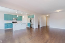 This property features a kitchen with teal cabinetry, stainless steel appliances, and a white island with a sink, all complemented by dark hardwood flooring throughout the open living area - 