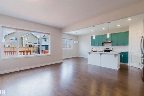 Open concept living area with hardwood floors, large windows, and a kitchen featuring teal cabinetry, a kitchen island, and stainless steel appliances - 4875 Wright Drive, Edmonton, AB - Indoor