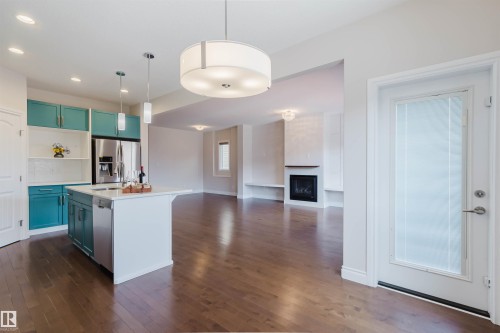 Open concept living space featuring hardwood floors, a kitchen island with pendant lighting, a stainless steel refrigerator, and a fireplace - 4875 Wright Drive, Edmonton, AB - Indoor Photo Showing Kitchen With Upgraded Kitchen
