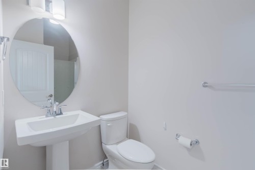 The bathroom features a pedestal sink with a contemporary faucet, an oval mirror, and a toilet - 4875 Wright Drive, Edmonton, AB - Indoor Photo Showing Bathroom