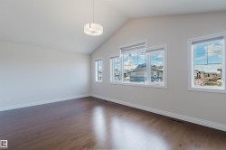 Spacious room featuring vaulted ceilings, a contemporary ceiling fixture, hardwood floors, and large windows providing natural light - 