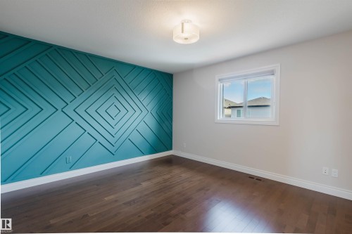 This room features a striking accent wall with a geometric pattern, dark hardwood floors, and a window providing natural light - 4875 Wright Drive, Edmonton, AB - Indoor Photo Showing Other Room