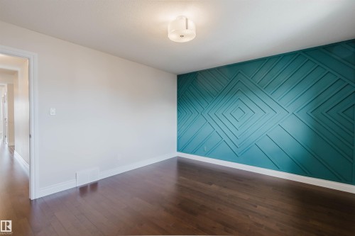 Room featuring dark hardwood flooring, a decorative accent wall with a geometric pattern, and a ceiling-mounted light fixture - 4875 Wright Drive, Edmonton, AB - Indoor Photo Showing Other Room